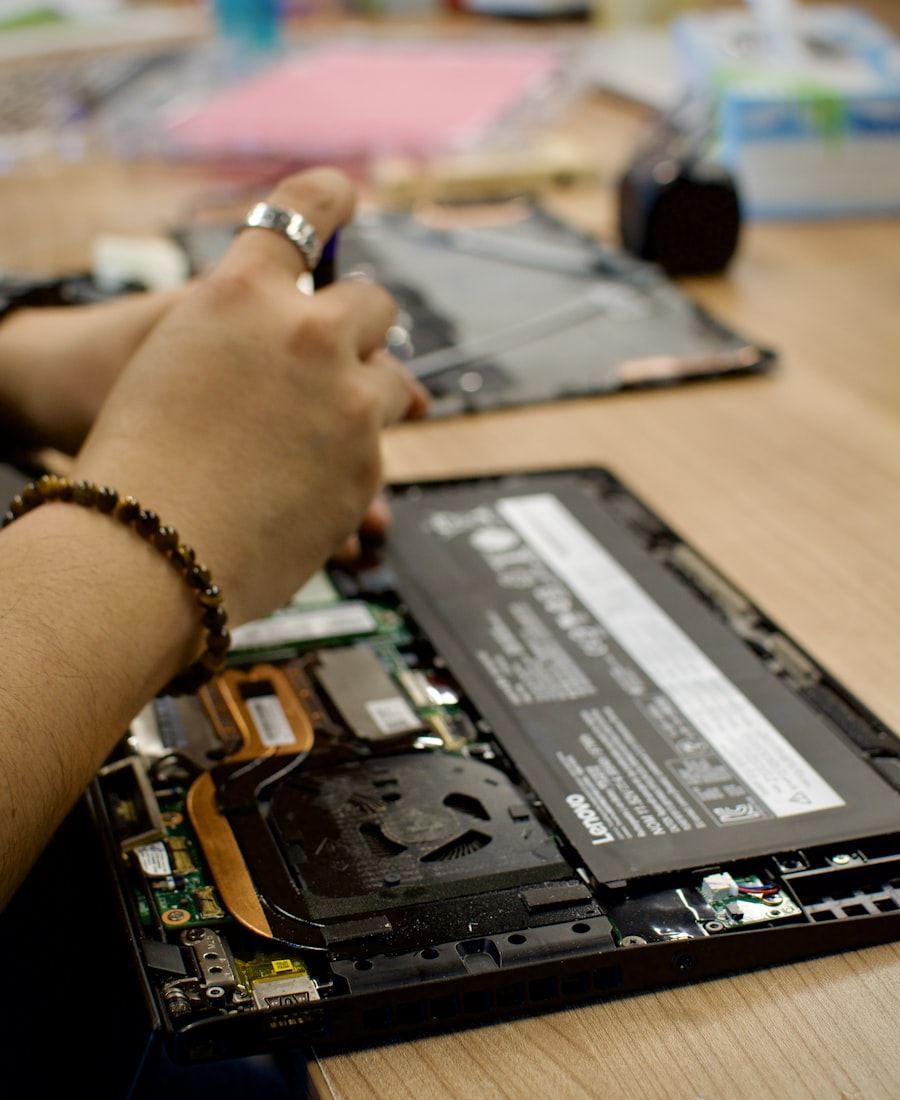 Hands working on the internals of an opened laptop at a wooden bench.